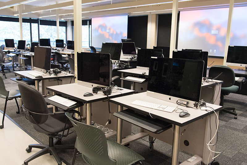 Room with many desktop computers and two large projector screens.