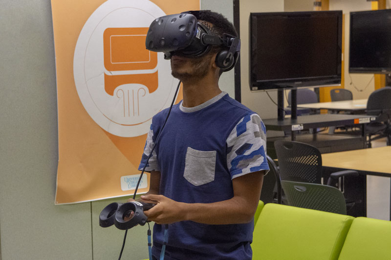 A student is using a VR headset with his hands on the visor while an instructor stands off to the side.