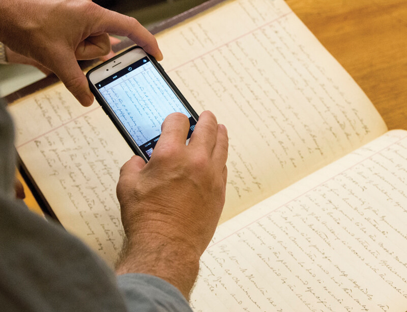 person holding a smartphone taking photos of the contents of a book