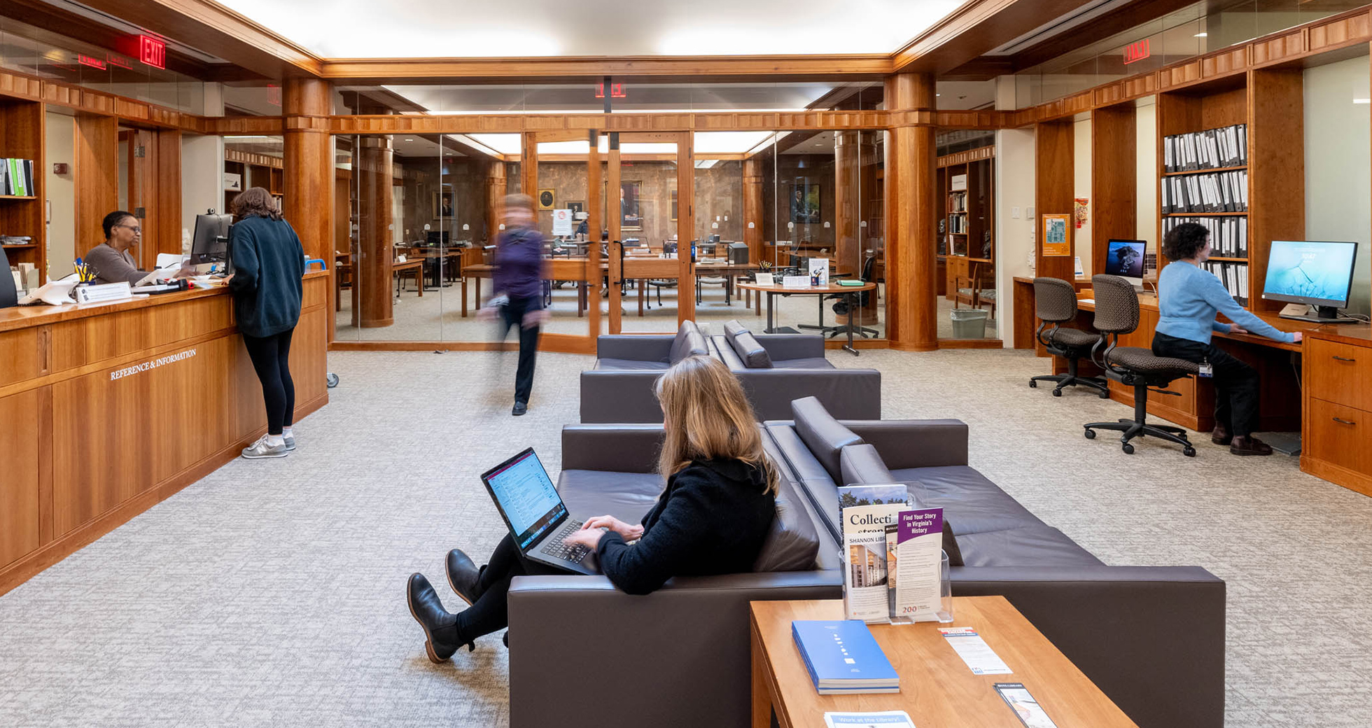 People enjoy a calm, airy room with couches, computers, and a large desk on the left side. An inner room is visible with more tables and chairs.