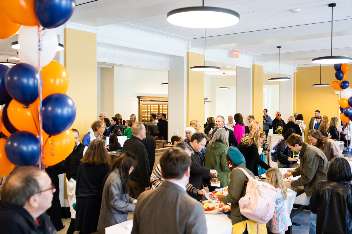 Guests attending an event in a brightly lit library room decorated with orange and blue balloons.