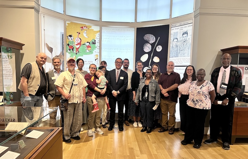 Group photo of several individuals posing in a seminar room with banners and displays related to historical texts and illustrations.