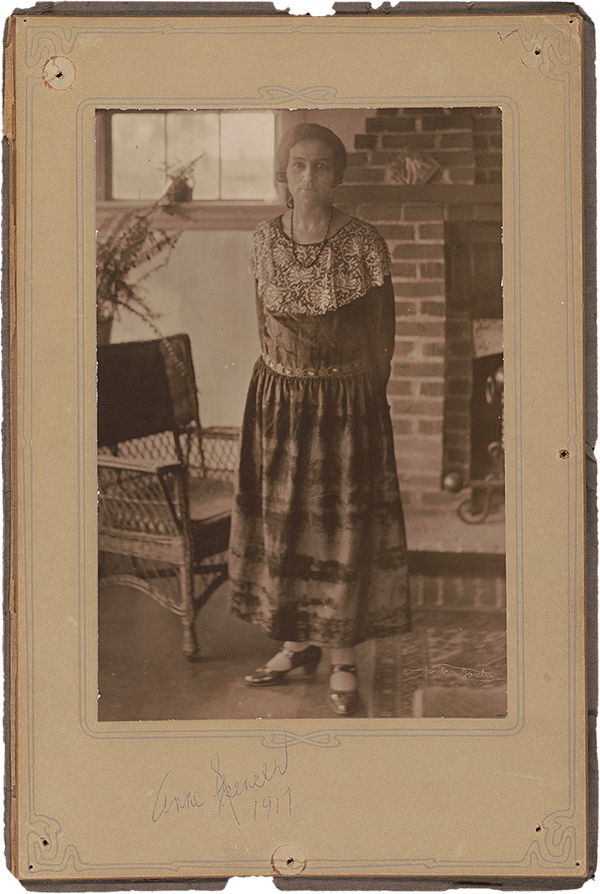 A woman in a dress stands in front of a brick fireplace