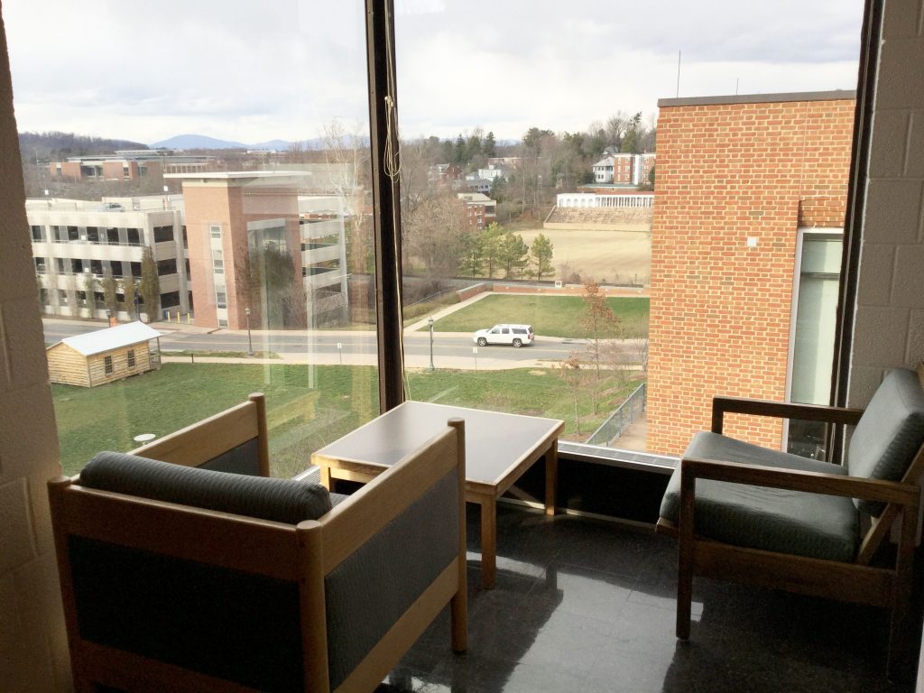 Cushioned chairs around a small, square table, facing a windowpanes forming one corner of the library.