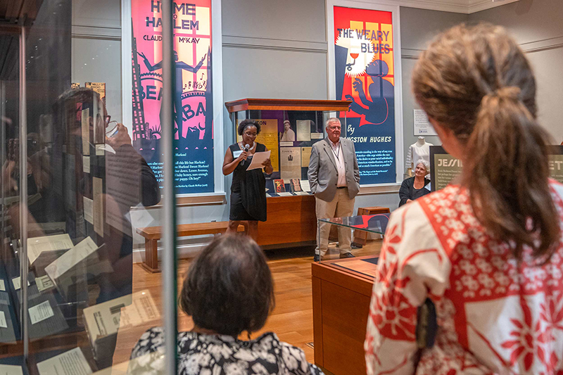 A woman in the Halrem Renaissance exhibition gallery speaks into a microphone as a crowd observes her.