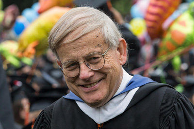 Sandy Gilliam wearing academic regalia, smiling at an outdoor event with colorful balloons in the background.