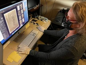 A person wearing white gloves works at a computer screen showing the negative image of a man in a military uniform