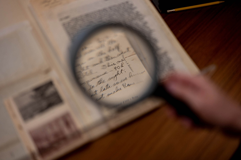 A person holds a magnifying glass up to an old handwritten text