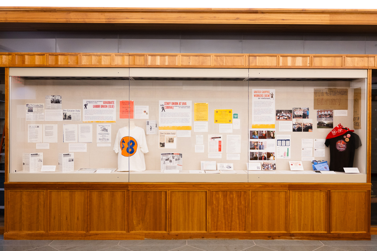 A front view of an exhibition case shows memorabilia, flyers, and protest signs related to labor organizing.