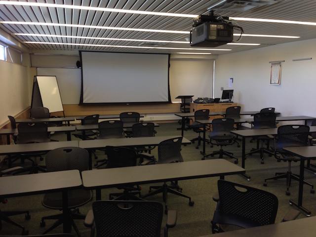 A large room with tables and a large screen at one end of the room