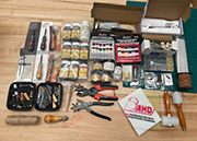 Assorted crafting tools and supplies laid out on a workbench, including jewelry making kits, scissors, pliers, and materials such as beads and threads, with a logo of "Artistic Wire" visible.